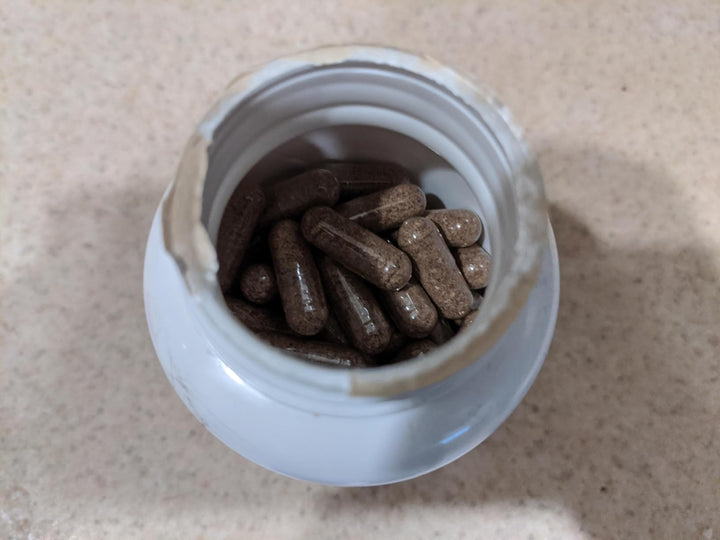 Open supplement bottle filled with brown capsules