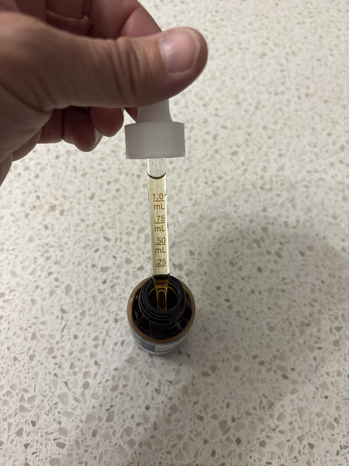 Measured liquid dropper held above an amber supplement bottle