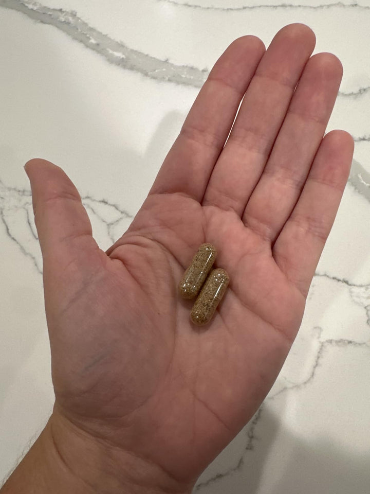Two brown supplement capsules held in a hand