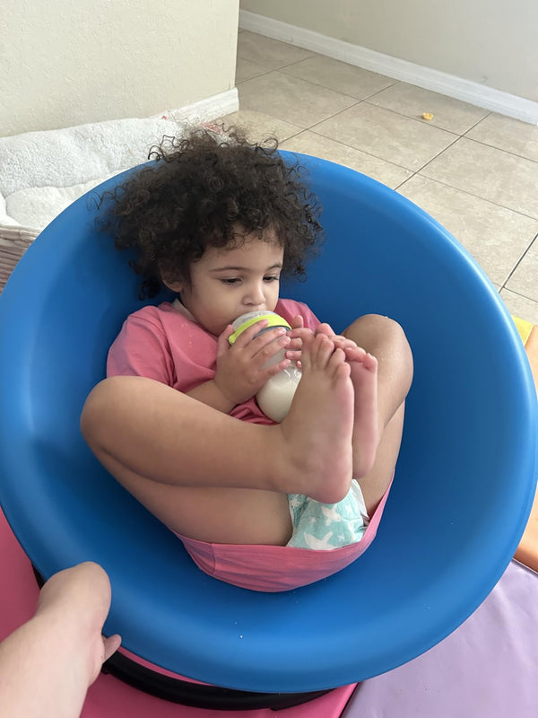 Young child drinking from a bottle while seated in a blue chair